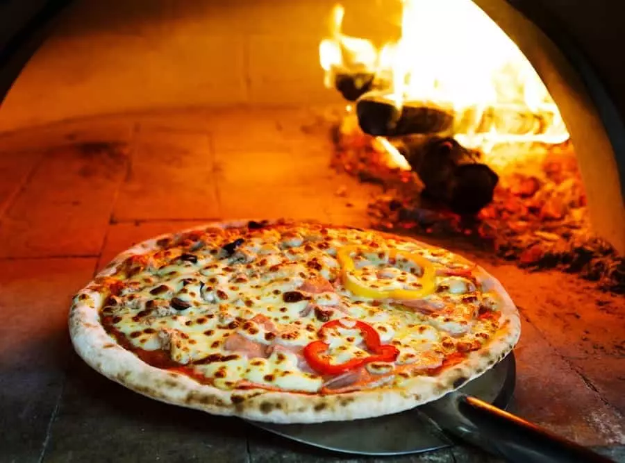 Pizza coming out of a brick oven with flames in background