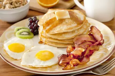 Pancakes with bacon, eggs, and fruit.