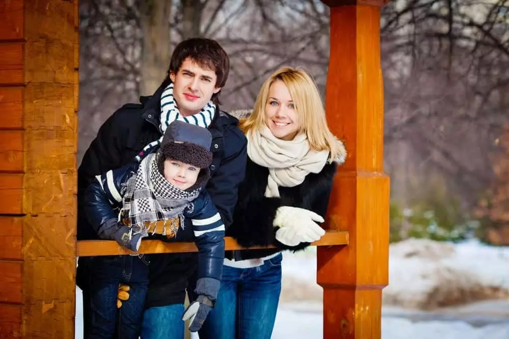 A young family in winter clothing standing on their cabin's porch.