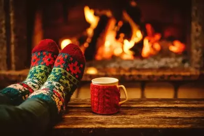 A pair of feet in wool socks relaxing in front of the fireplace with a mug in a cabin.