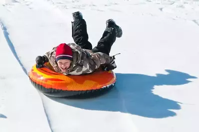 A smiling boy snow tubing down a mountain.